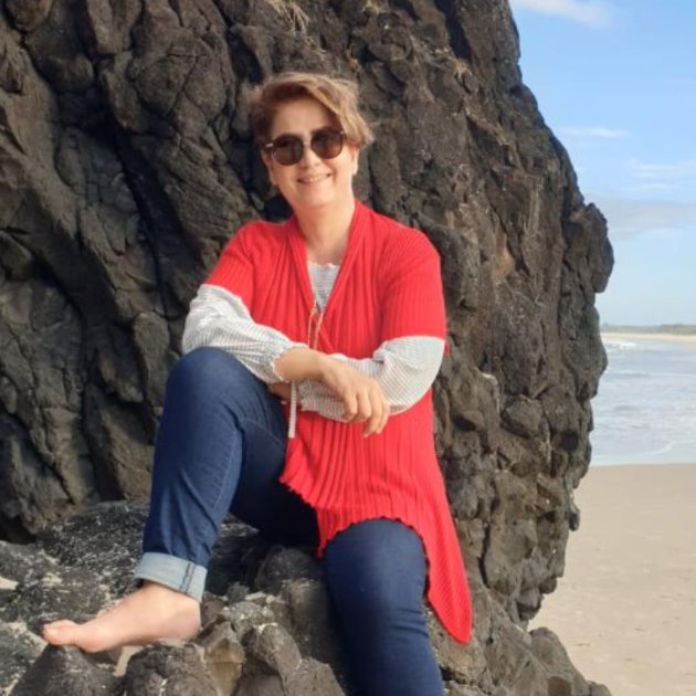 Person in red sweater sitting by a rocky coast.