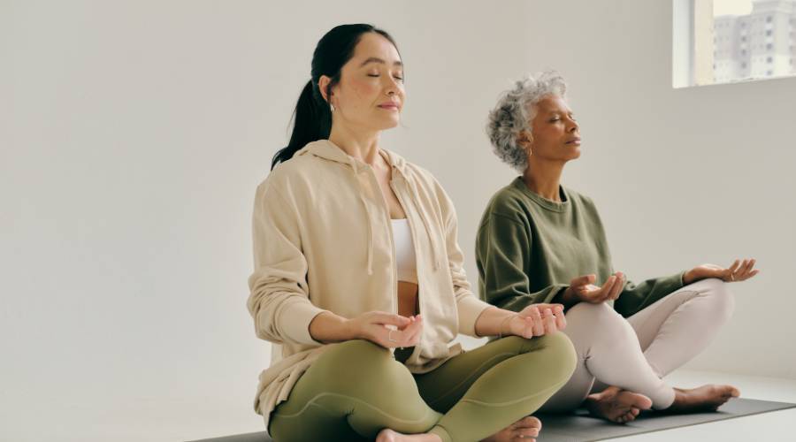 Two women meditating on yoga mats in serene setting.